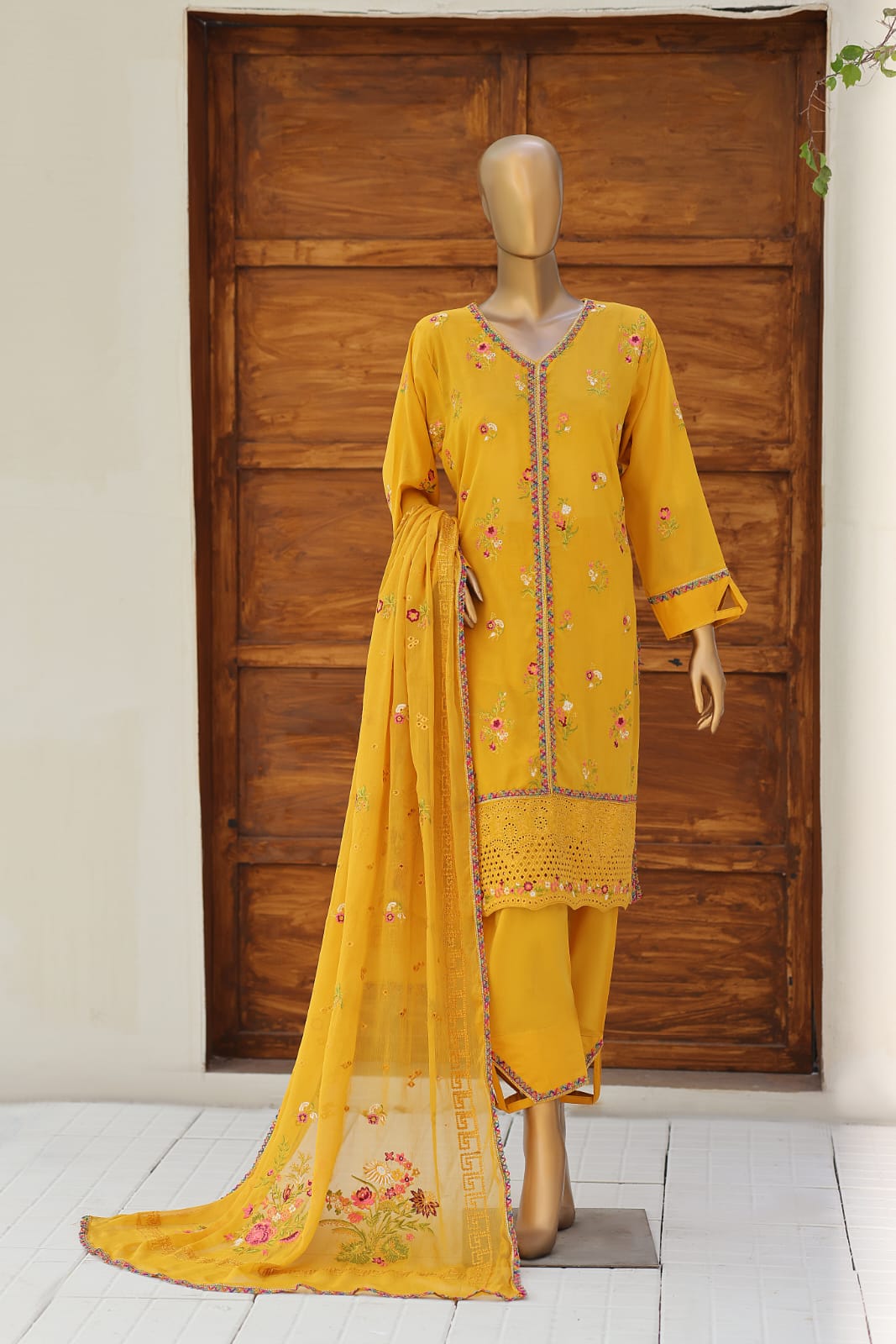 Yellow embroidered traditional outfit on a mannequin in front of a wooden door.