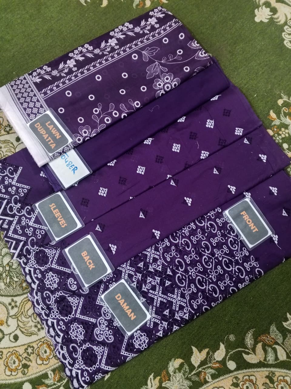 Purple fabric with white patterns and brand labels on a green patterned surface