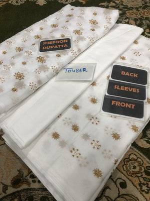White dupatta with gold patterns and labels on a textured surface