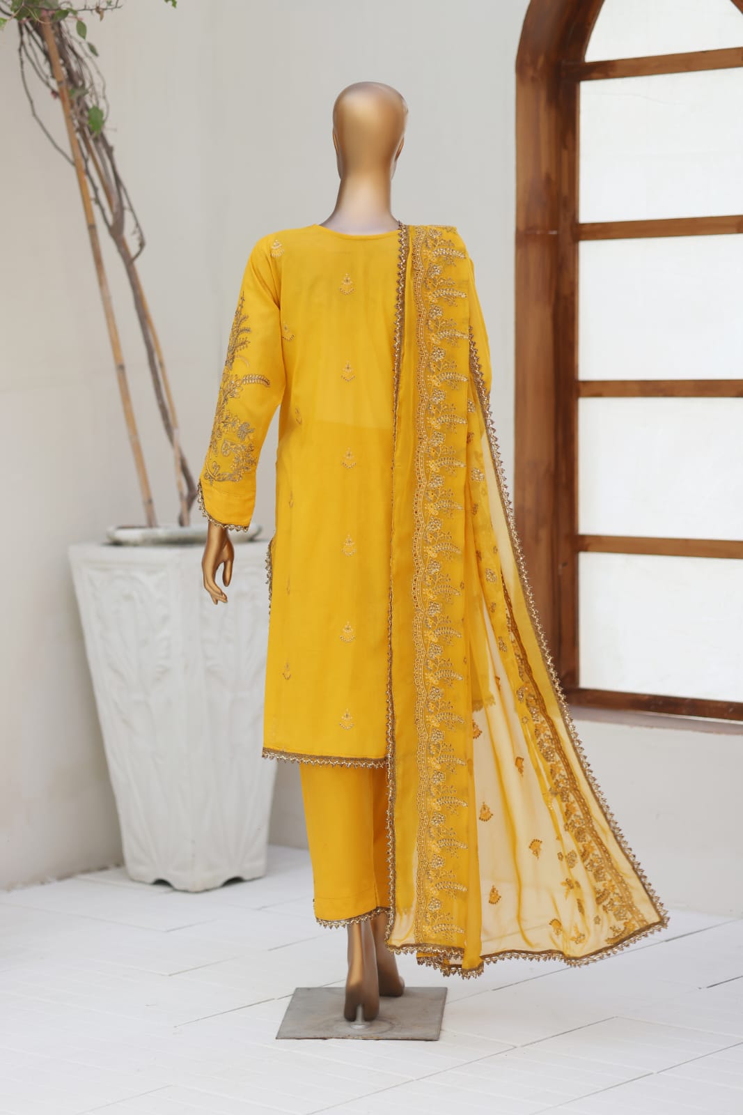 Yellow embroidered outfit on a mannequin against a white wall with a plant in the background