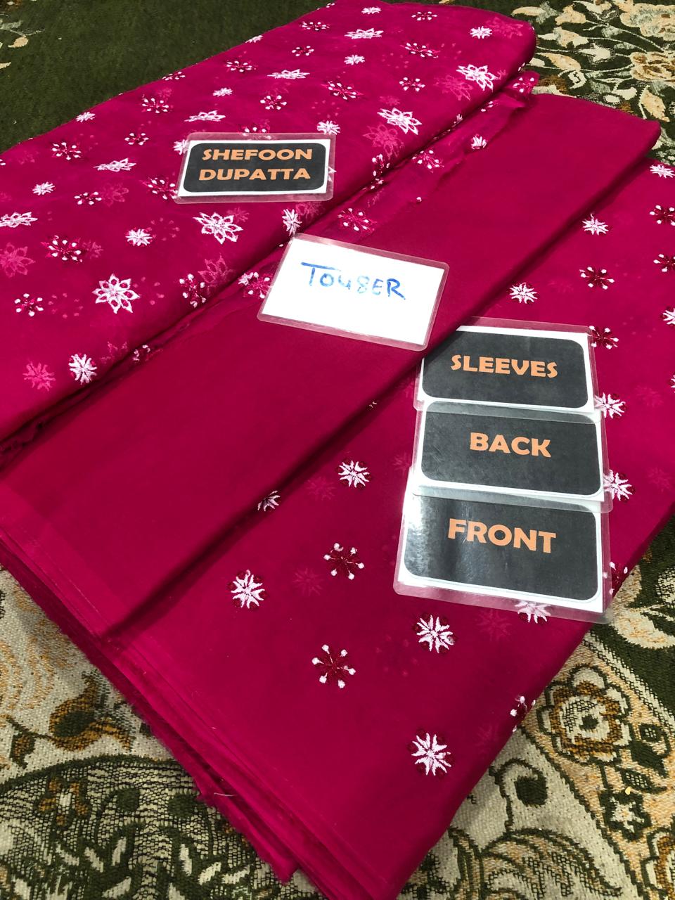 pink dupatta with white patterns, tags indicating size and direction, on a patterned surface.