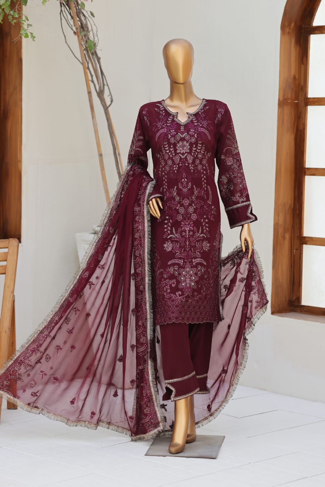 Maroon embroidered outfit with a sheer dupatta on a mannequin against a white wall.