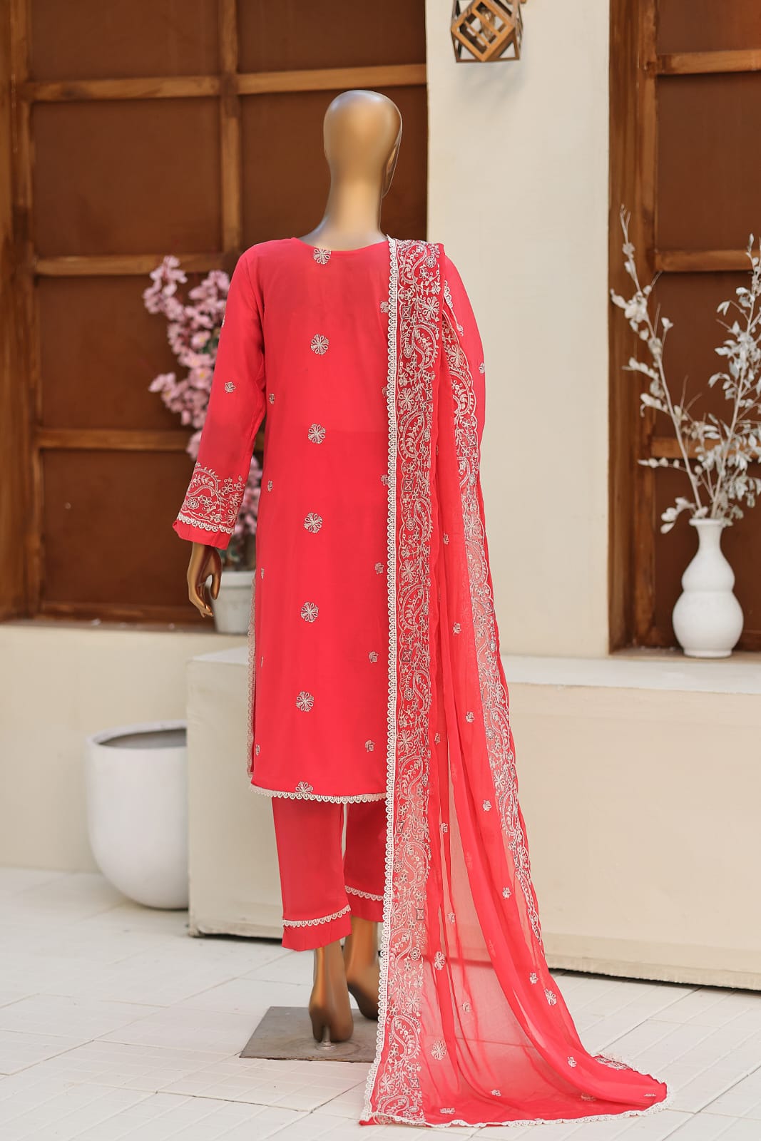 Red traditional outfit with intricate patterns on a mannequin against a neutral background.